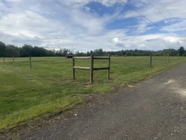 Wooden post-and-rail horse fence corner along a gravel driveway